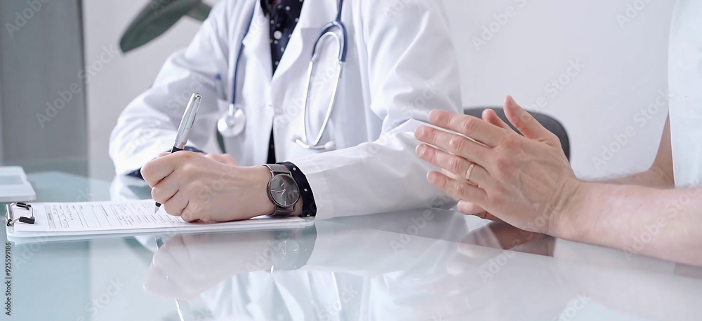 Doctor consulting patient in clinic. Female physician is writing notes while talking with a man, close up. Medicine concept Doctor consulting patient in clinic. Female physician is writing notes while talking with a man, close up. Medicine concept