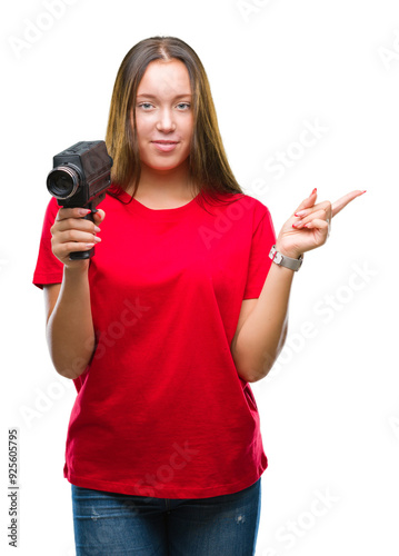 Young beautiful caucasian woman filming using vintage video camera over isolated background very happy pointing with hand and finger to the side