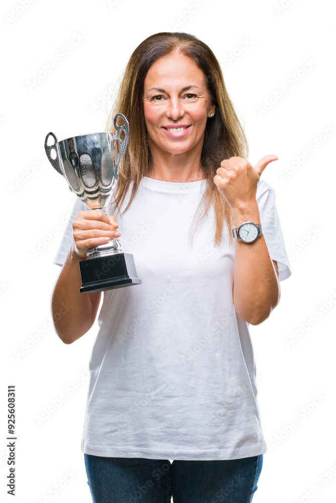Middle age hispanic winner woman celebrating award holding trophy over isolated background pointing and showing with thumb up to the side with happy face smiling Middle age hispanic winner woman celebrating award holding trophy over isolated background pointing and showing with thumb up to the side with happy face smiling