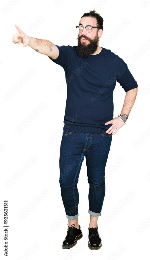 Young hipster man with long hair and beard wearing glasses Pointing with finger surprised ahead, open mouth amazed expression, something in front Young hipster man with long hair and beard wearing glasses Pointing with finger surprised ahead, open mouth amazed expression, something in front