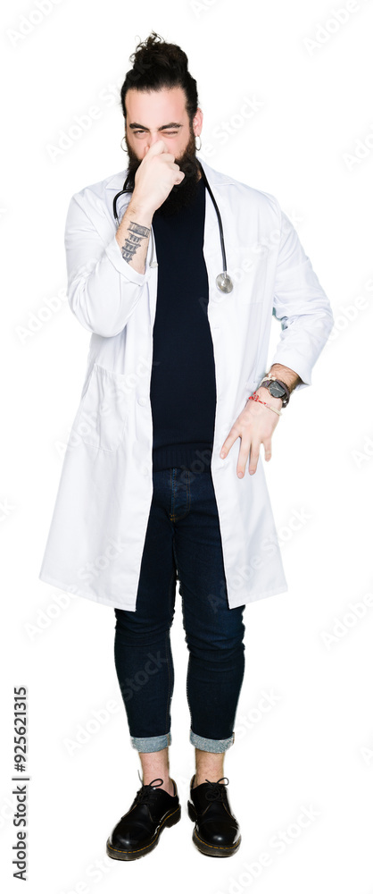 Doctor with long hair wearing medical coat and stethoscope smelling something stinky and disgusting, intolerable smell, holding breath with fingers on nose. Bad smells concept. Doctor with long hair wearing medical coat and stethoscope smelling something stinky and disgusting, intolerable smell, holding breath with fingers on nose. Bad smells concept.