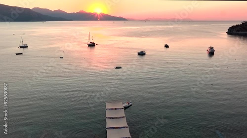 A serene scene of a calm bay at sunset, featuring anchored boats and a wooden pier extending into the tranquil waters, all bathed in the warm glow of the setting sun. photo