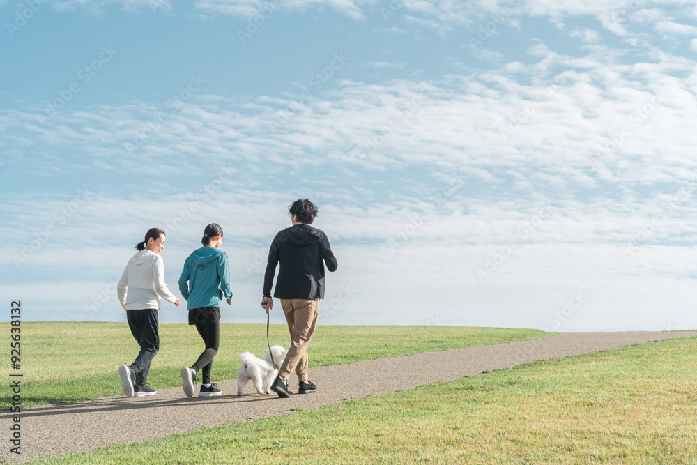 Obraz premium 青空の見える公園で犬の散歩・運動・トレーニング・有酸素運動をするさわやかな家族・親子 