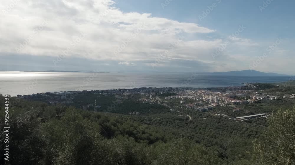 A picturesque view of a coastal town nestled between lush green hills and the shimmering sea under a partly cloudy sky. A picturesque view of a coastal town nestled between lush green hills and the shimmering sea under a partly cloudy sky.