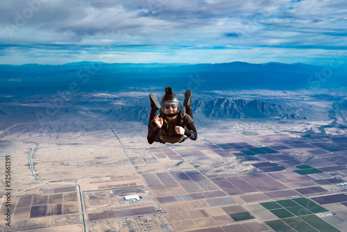 Waving and smiling woman makes skydive alone over Arizona desert with mountains and dramatic clouds