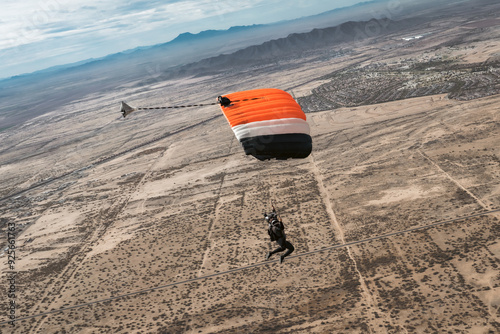 Woman flying orange parachute over the desert with mountains and clouds