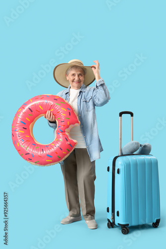 Senior female tourist with swim ring and suitcase on blue background