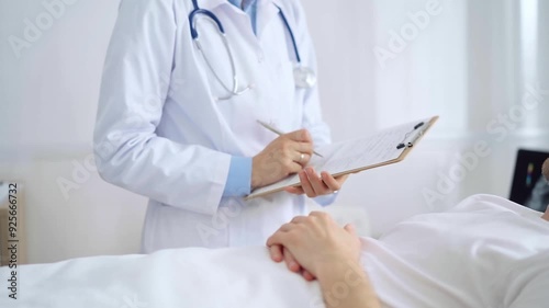 Female doctor writing medical report of patient lying in bed in hospital