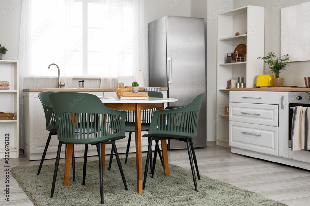 Fototapeta premium Interior of light kitchen with fridge, white counters with oven and dining table