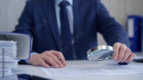 Businessman is carefully examining financial documents with a magnifying glass, highlighting the importance of thorough analysis in business. Audit and taxes photo