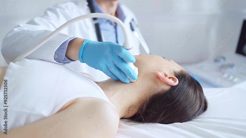 Doctor man wearing blue medical gloves is using ultrasound equipment on neck of female patient lying down for a medical examination Doctor man wearing blue medical gloves is using ultrasound equipment on neck of female patient lying down for a medical examination