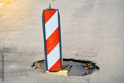 Deteriorated asphalt road surface, pothole marked with caution sign for public safety. Traffic hazard alert. Road barricade, dangerous pothole. Pothole with warning sign signals photo