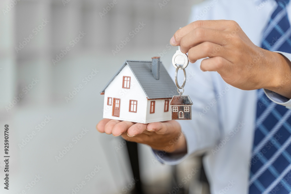 Close up hands of a realtor holding house key chaing and a small house model, buying home or real estate concept Close up hands of a realtor holding house key chaing and a small house model, buying home or real estate concept