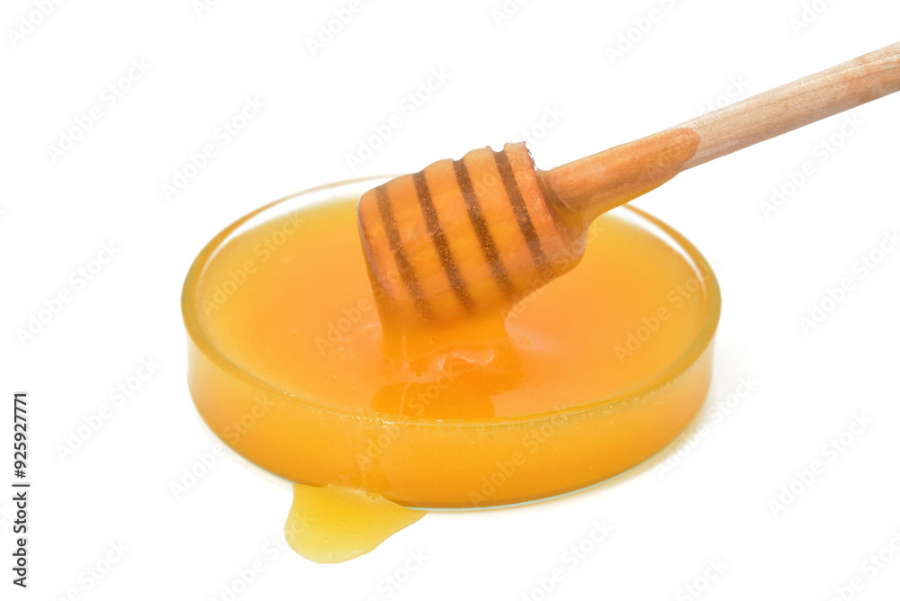 Honey dripping from wooden honey dipper in the glass bowl. Isolated on the white background. Close-up. Copy space. Selective focus. Honey dripping from wooden honey dipper in the glass bowl. Isolated on the white background. Close-up. Copy space. Selective focus.