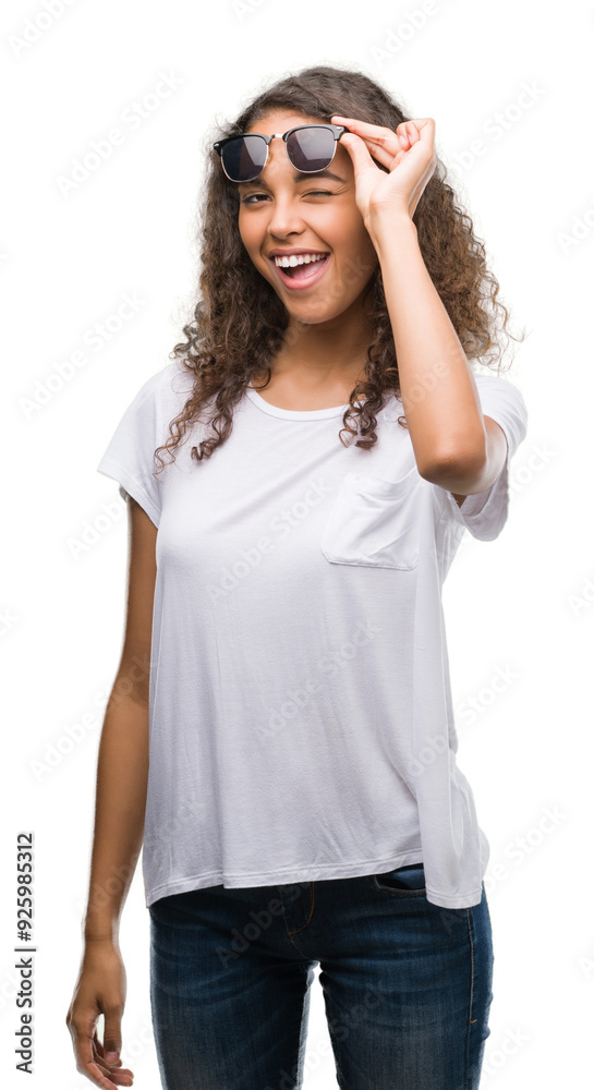 Young hispanic woman wearing sunglasses winking looking at the camera with sexy expression, cheerful and happy face.