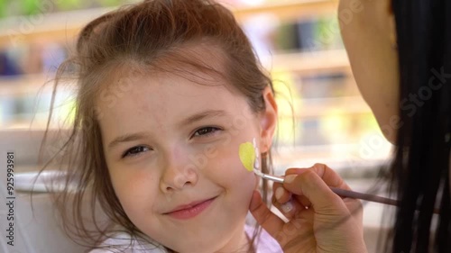 The artist makes a drawing on the girl's face with a face painting. 