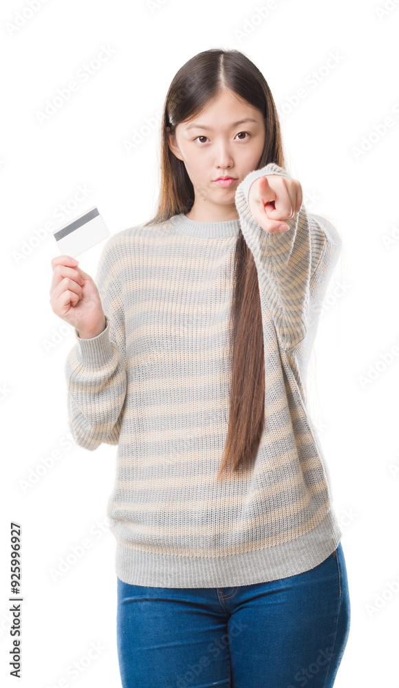 Young Chinese woman over isolated background holding credit card pointing with finger to the camera and to you, hand sign, positive and confident gesture from the front Young Chinese woman over isolated background holding credit card pointing with finger to the camera and to you, hand sign, positive and confident gesture from the front