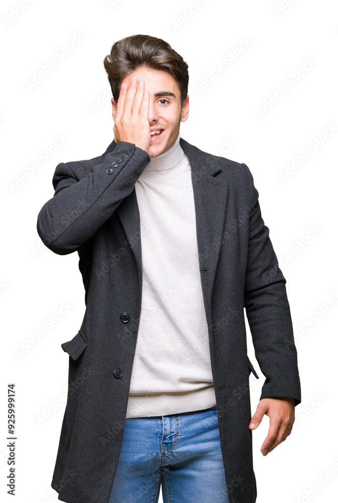 Young elegant man wearing winter coat over isolated background covering one eye with hand with confident smile on face and surprise emotion. Young elegant man wearing winter coat over isolated background covering one eye with hand with confident smile on face and surprise emotion.