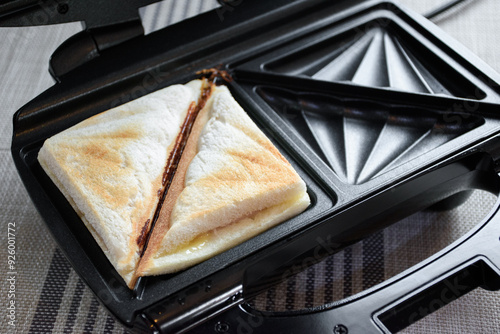 Close up of hot sandwich ham and cheese on a toaster for making hot sandwich toast breakfast. Bread and toaster on the kitchen table.