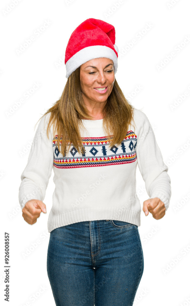 Middle age adult woman wearing winter sweater and chrismat hat over isolated background celebrating surprised and amazed for success with arms raised and open eyes. Winner concept. Middle age adult woman wearing winter sweater and chrismat hat over isolated background celebrating surprised and amazed for success with arms raised and open eyes. Winner concept.