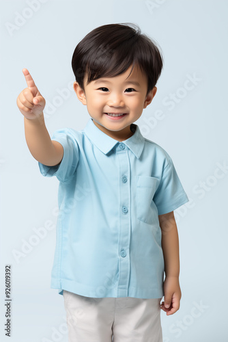 young Asian kid wearing a beige outfit is pointing at the camera, isolated on a white isolated background