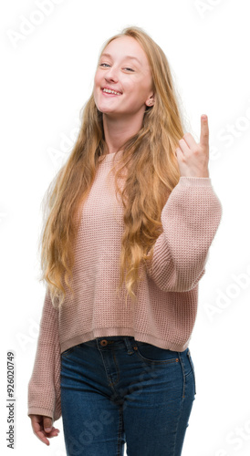 Blonde teenager woman wearing pink sweater showing and pointing up with finger number one while smiling confident and happy.