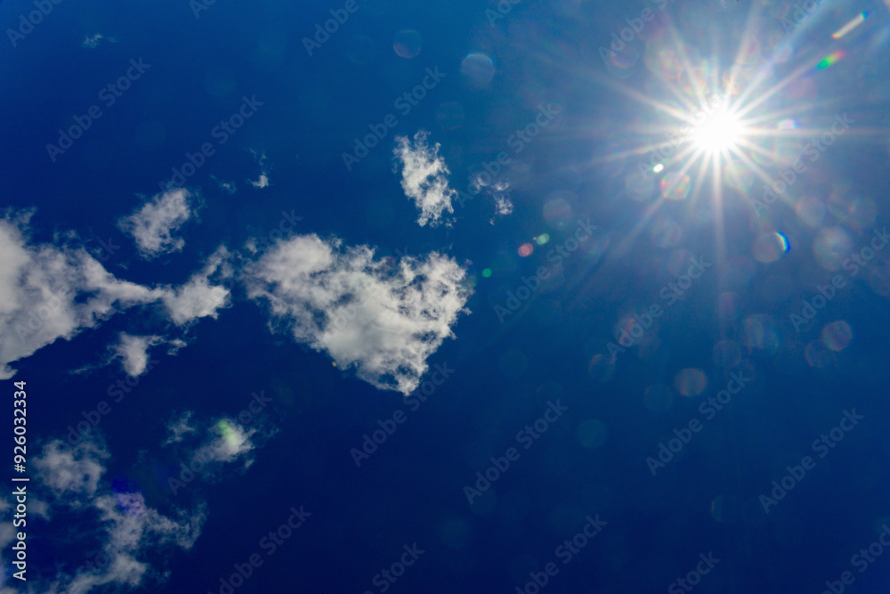 Blue sky with clouds and sun reflection.