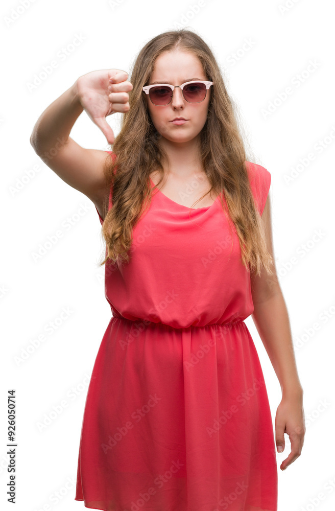 Young blonde woman wearing pink sunglasses with angry face, negative sign showing dislike with thumbs down, rejection concept Young blonde woman wearing pink sunglasses with angry face, negative sign showing dislike with thumbs down, rejection concept
