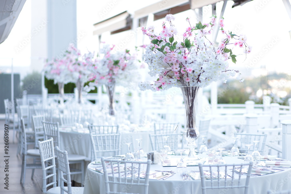 A minimalist and modern outdoor wedding reception with round tables and tall floral centerpieces. The flowers are a mix of pink and white, creating a clean and fresh look