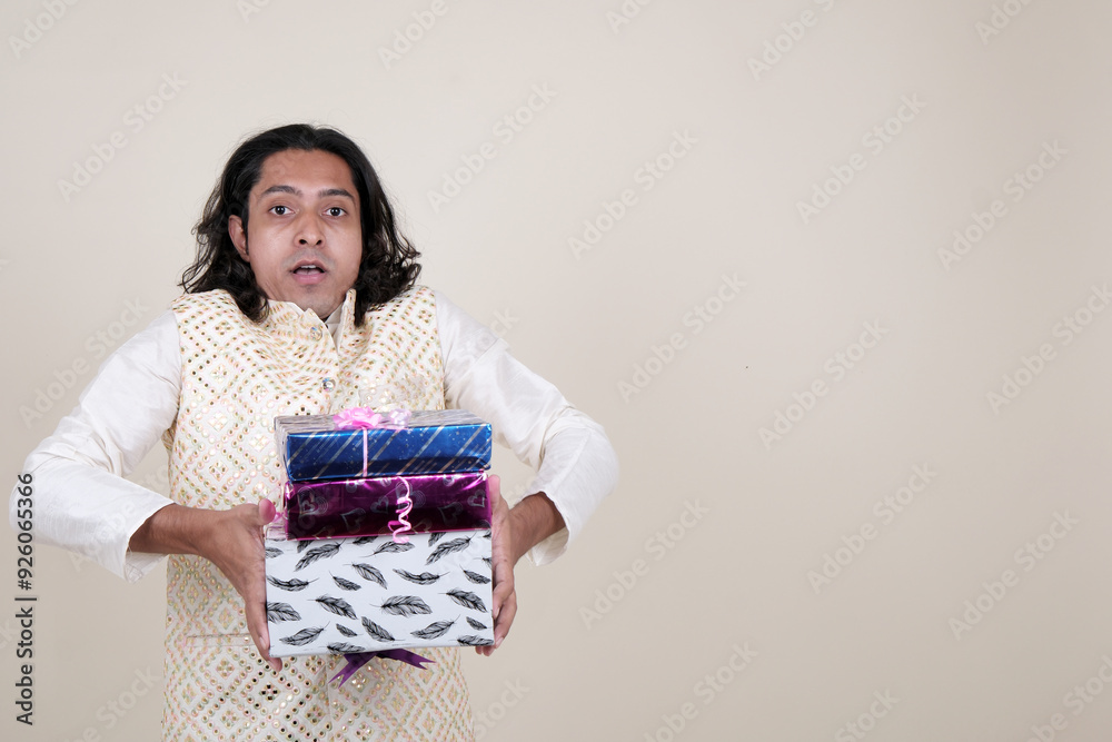 A happy young man in traditional attire, holding gift boxes and looking at the camera against a cream background. A happy young man in traditional attire, holding gift boxes and looking at the camera against a cream background.