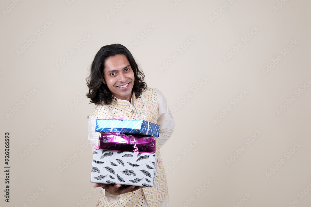A happy young man in traditional attire, holding gift boxes and looking at the camera against a cream background. A happy young man in traditional attire, holding gift boxes and looking at the camera against a cream background.