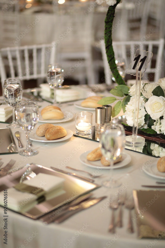 A close-up of a wedding table setting with white flowers, candles, and mirrored placemats. The table is set for a formal dinner