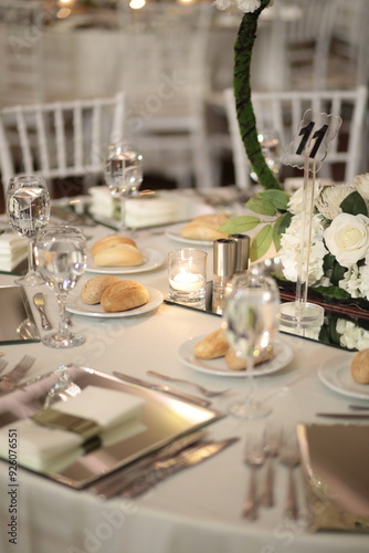 Obraz na płótnie A close-up of a wedding table setting with white flowers, candles, and mirrored placemats. The table is set for a formal dinner w salonie