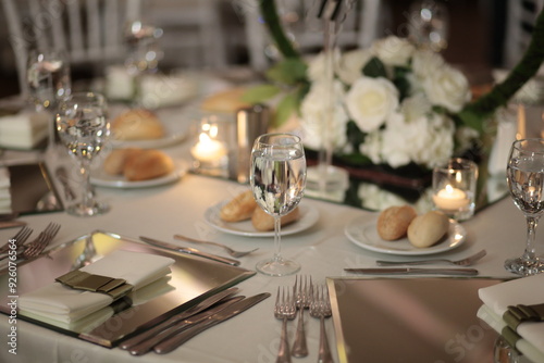 A close-up of a wedding table setting with white flowers, candles, and mirrored placemats. The table is set for a formal dinner