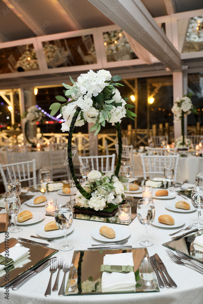 A beautifully decorated wedding table with white flowers, crystal glassware, and candles. The table is set with elegant place settings and a mirrored runner A beautifully decorated wedding table with white flowers, crystal glassware, and candles. The table is set with elegant place settings and a mirrored runner