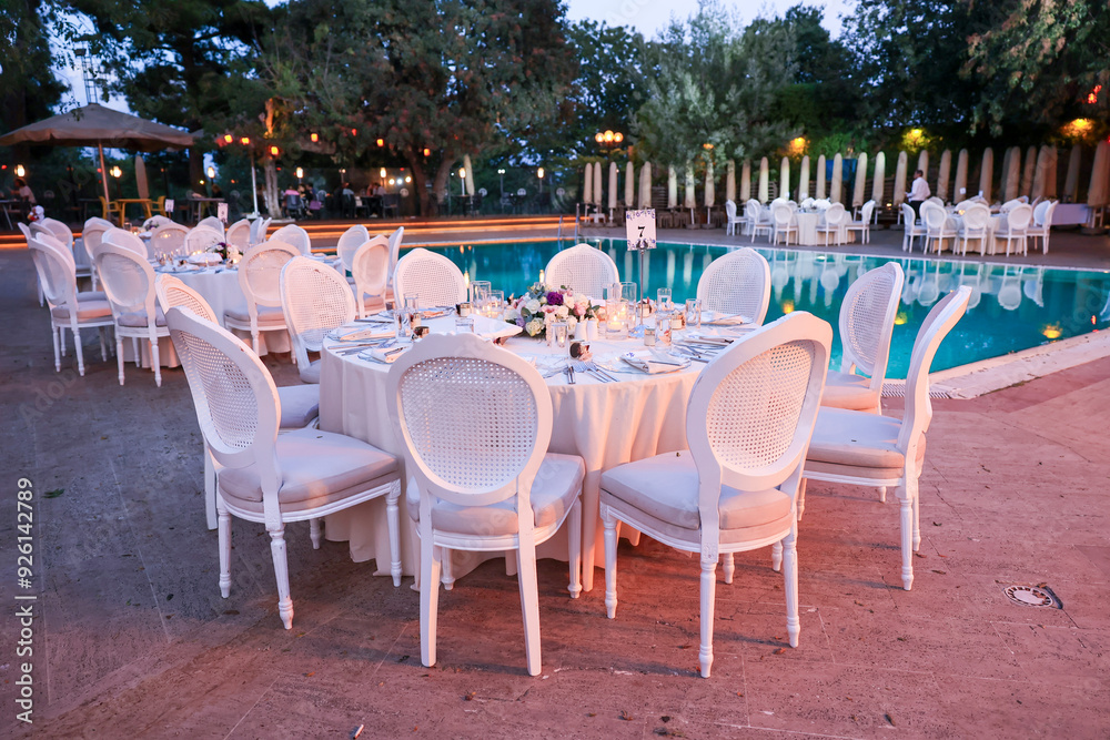 Outdoor Wedding Setup: Round Tables and Floral Decor by a Swimming Pool