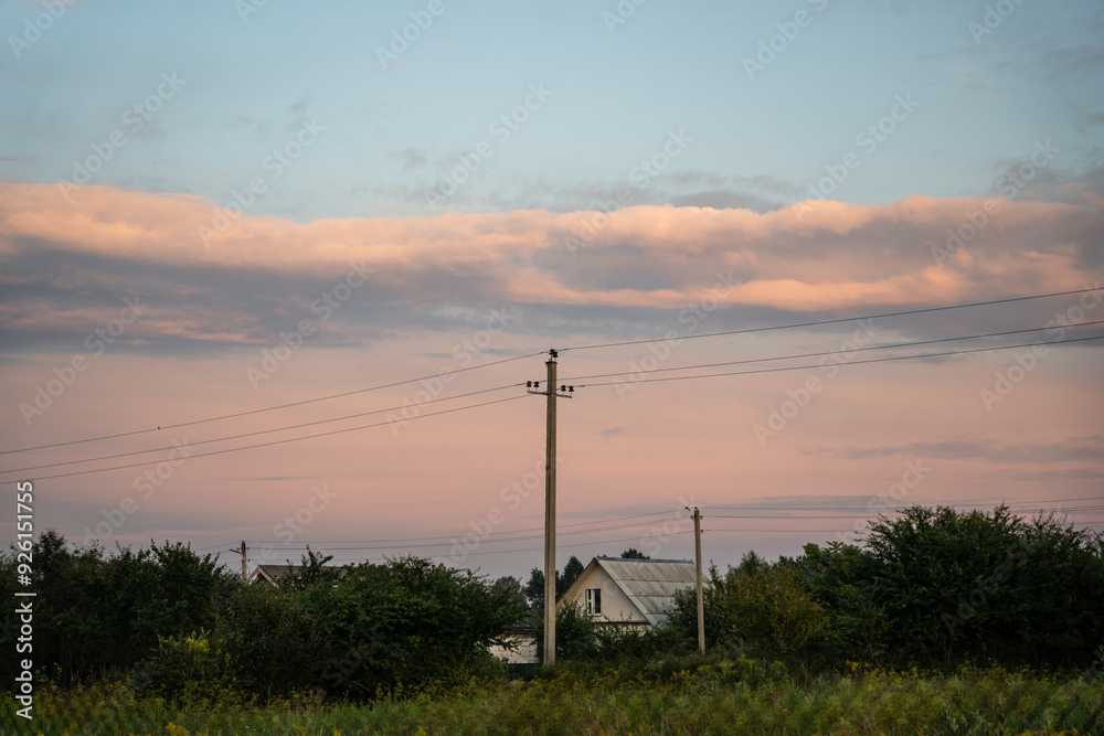 Obraz premium The support of power lines against the background of an orange sunset sky