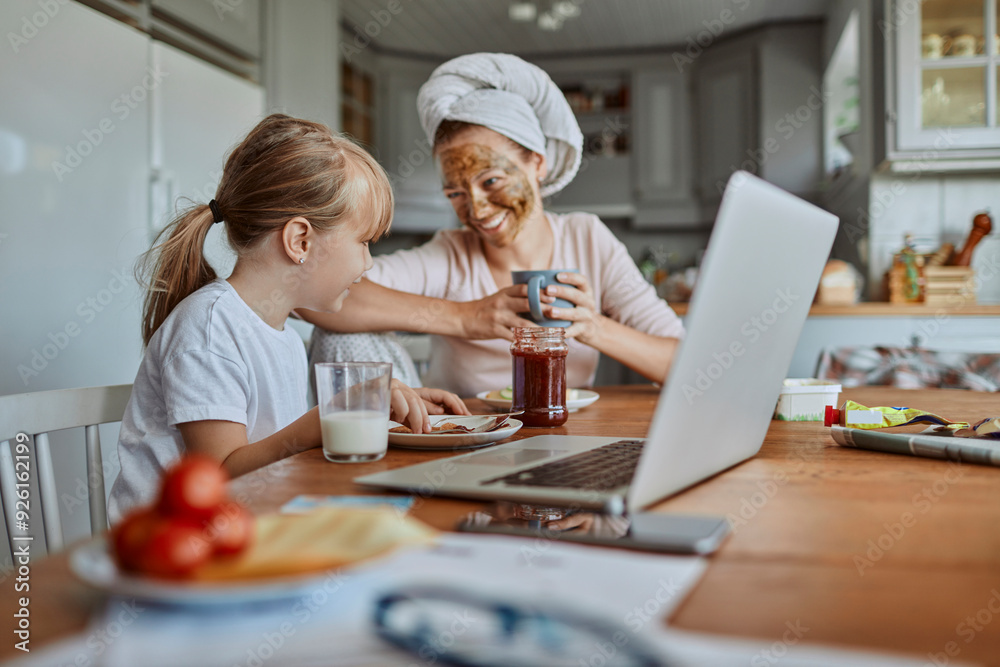 Happy mother and daughter having breakfast with laptop in kitchen Happy mother and daughter having breakfast with laptop in kitchen