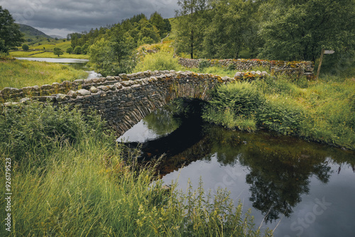Kleine Steinbrücke über einen schmalen Bach in grüner Hügellandschaft