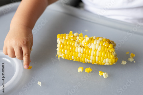 Baby picking sweet corn kernels from the table. Closeup. photo