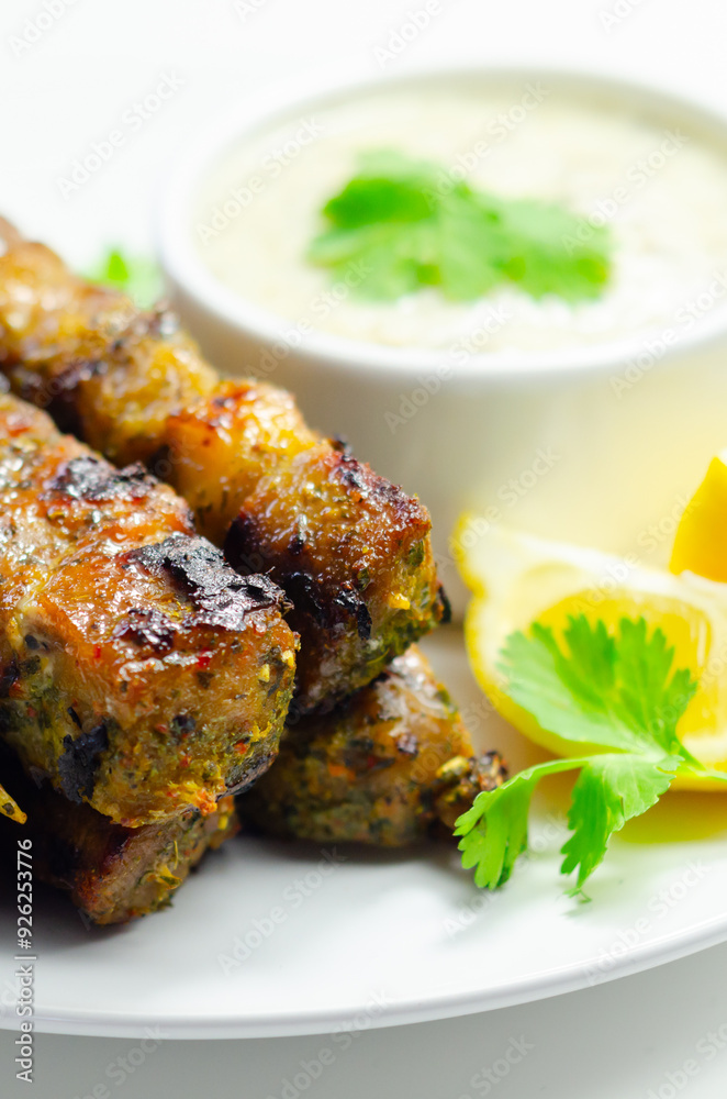 A plate of few skewers of meat with a side of sauce A plate of few skewers of meat with a side of sauce
