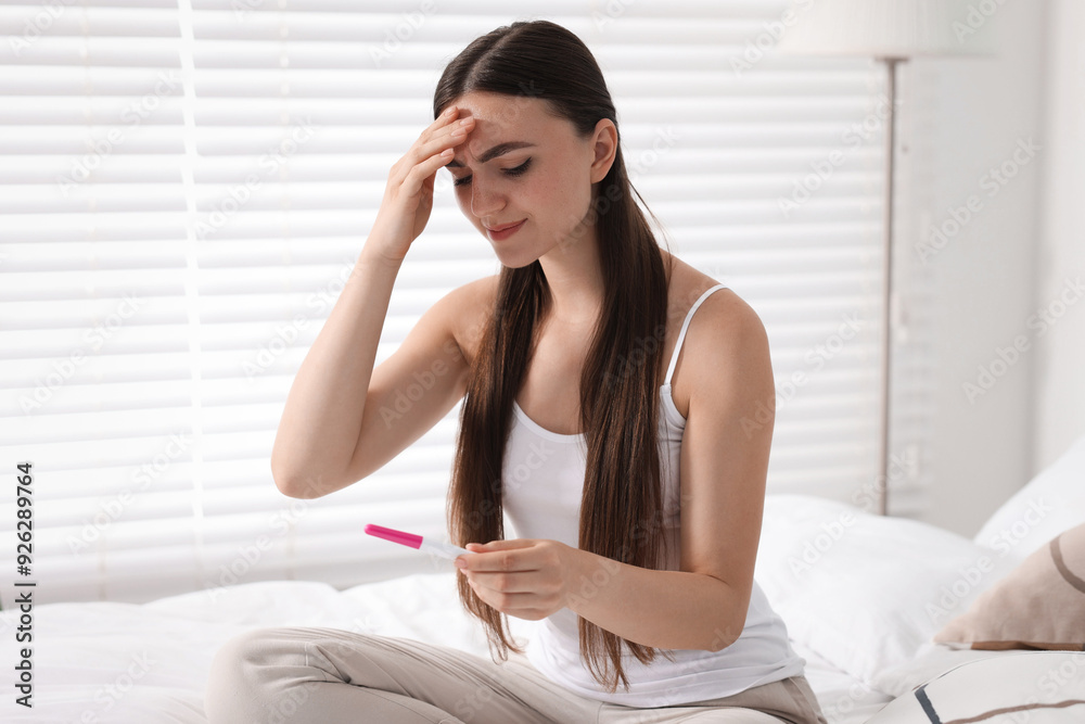 Sad woman holding pregnancy test on bed in room Sad woman holding pregnancy test on bed in room