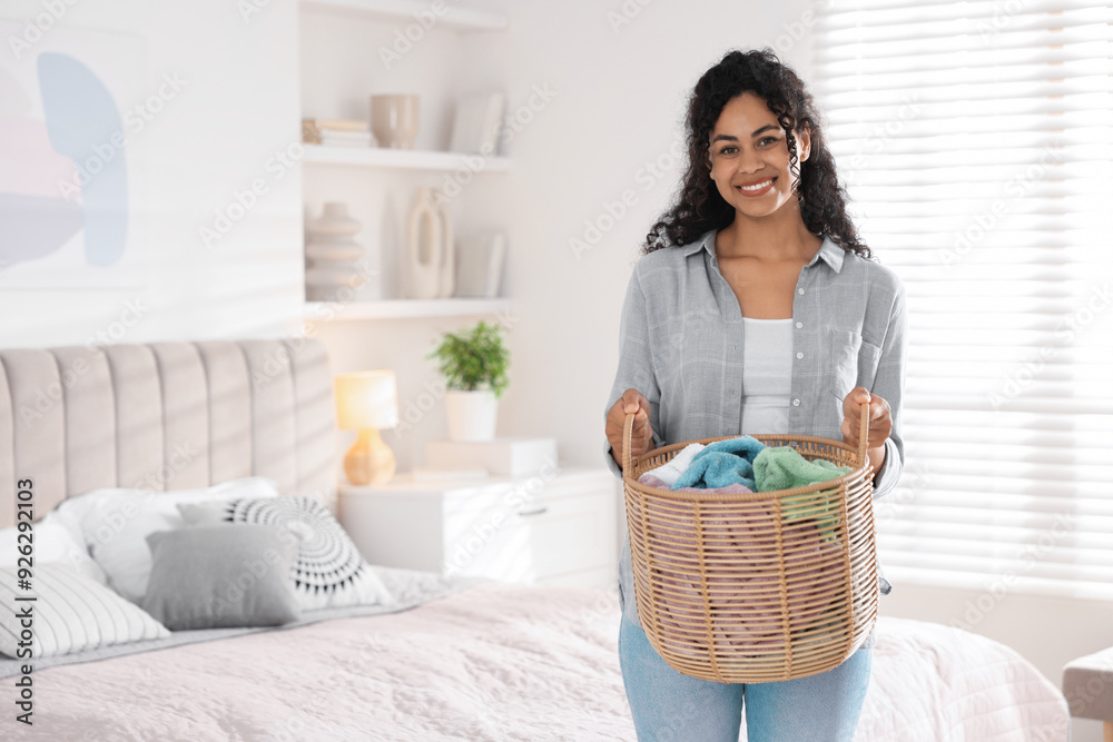 Happy woman with basket full of laundry in bedroom
