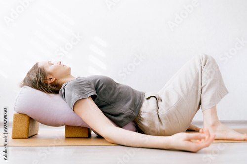 Woman in casual clothing doing yin/restorative yoga with bolster supported by blocks