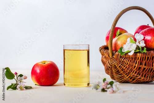 Still life, composition with sweet ripe red apple with apple fresh juice in glass with branch with flowers of apple tree. Basket with apples. Healthy vegan or vegetarian food, drink