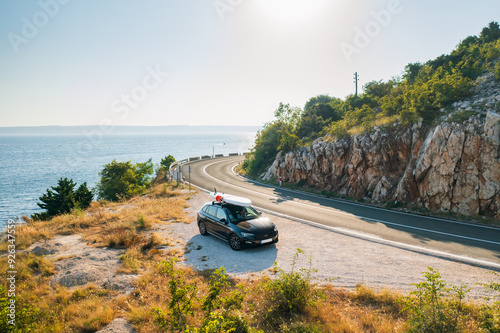 Canvas Print Black car with a paddleboard tightly secured atop its roof, parked in the side o