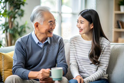 Asian adult daughter and senior father sitting on couch in living room at home enjoying a pleasant conversation