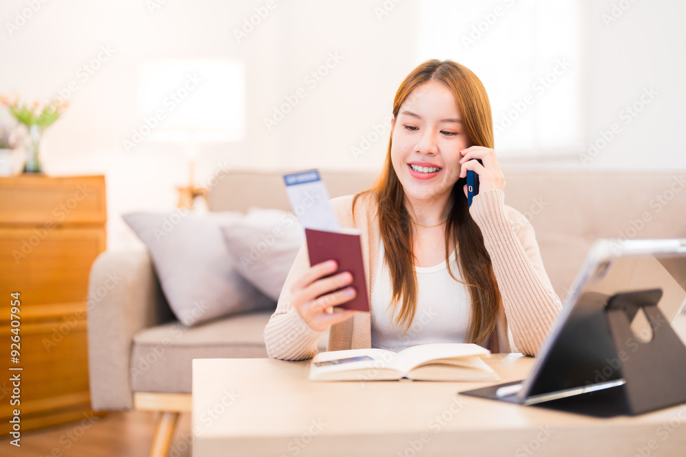 A young woman is sitting on the floor, talking on the phone and looking at her boarding pass, smiling as she prepares for a trip with her suitcase open beside her A young woman is sitting on the floor, talking on the phone and looking at her boarding pass, smiling as she prepares for a trip with her suitcase open beside her
