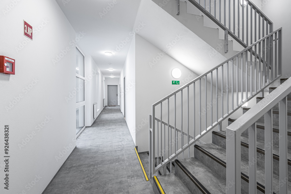 Modern hallway with stairs and metal railings in a bright building, featuring geometric lines and a long corridor leading to multiple doors. Modern hallway with stairs and metal railings in a bright building, featuring geometric lines and a long corridor leading to multiple doors.
