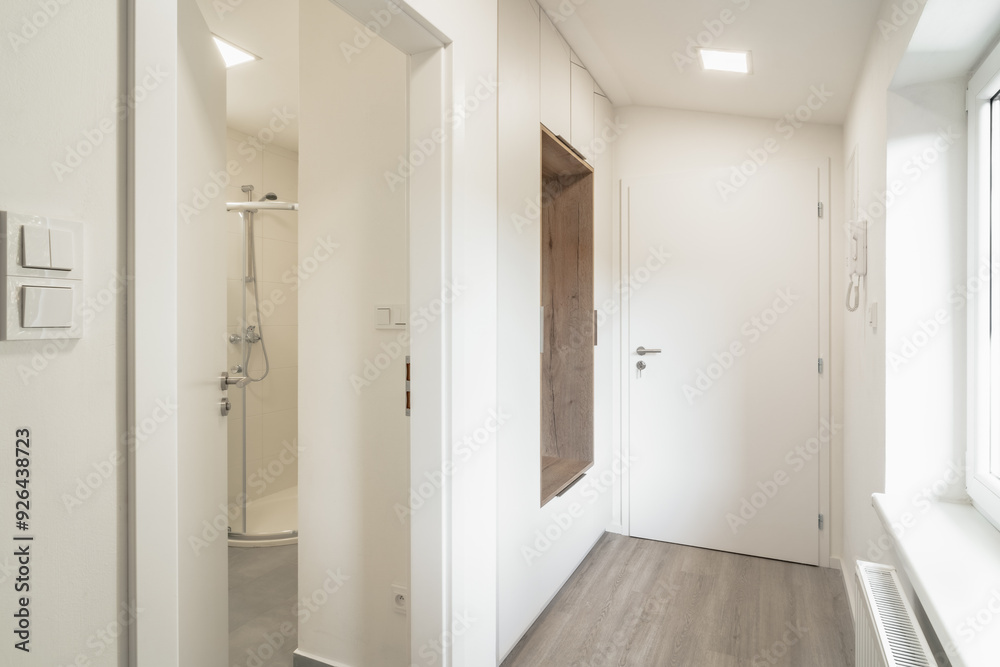 Bright and modern hallway in an apartment with a view into a small bathroom, featuring a minimalistic design, light-colored walls, and built-in closets. Bright and modern hallway in an apartment with a view into a small bathroom, featuring a minimalistic design, light-colored walls, and built-in closets.